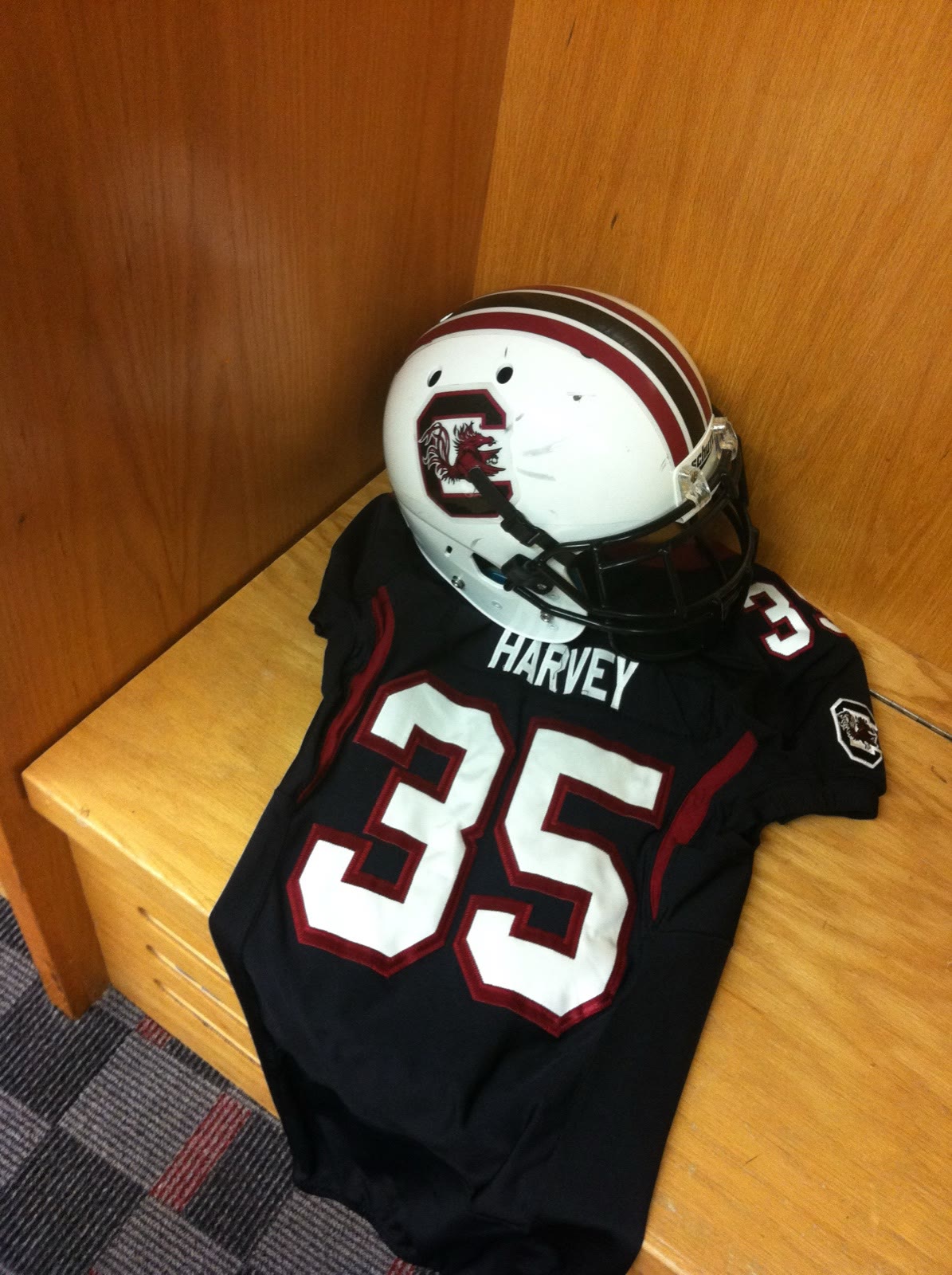 A South Carolina Gamecocks game jersey reading HARVEY 35, folded in a wooden locker beneath a game helmet